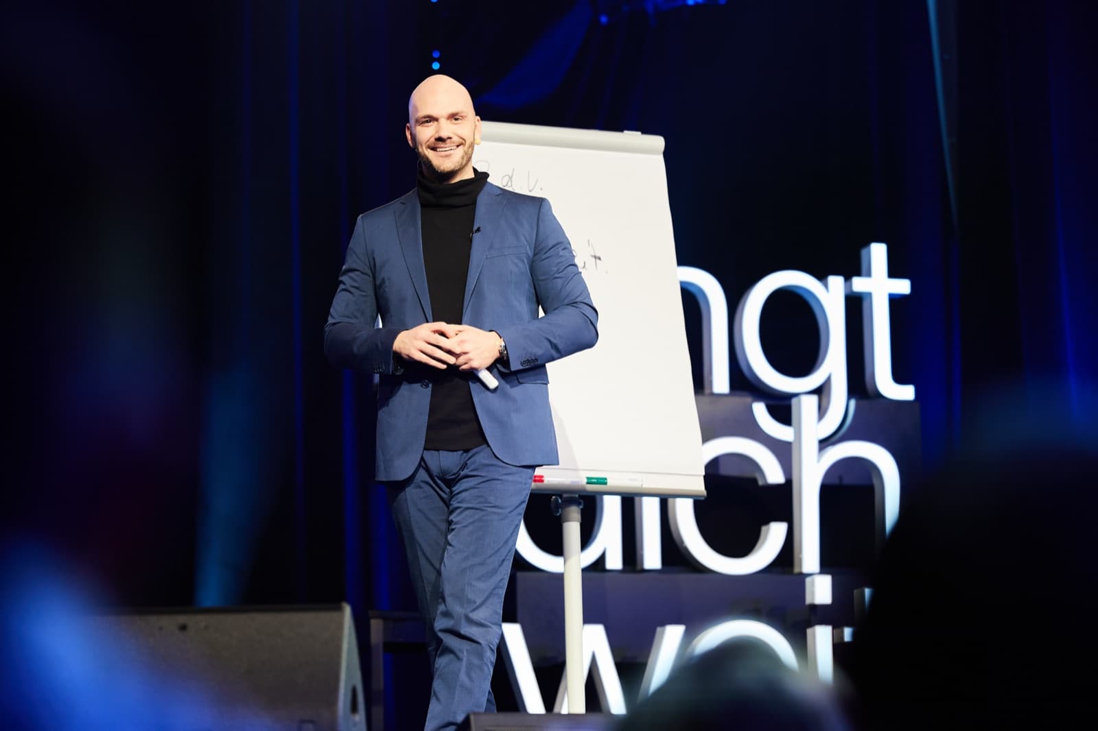 Mitch Rau lächelnd auf der Bühne neben einem Flipchart